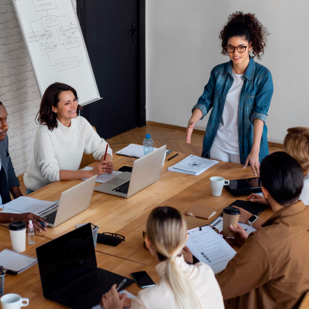 Team meeting with diverse professionals discussing strategies, laptops open, and a woman presenting ideas, emphasizing collaboration for effective SEO solutions.